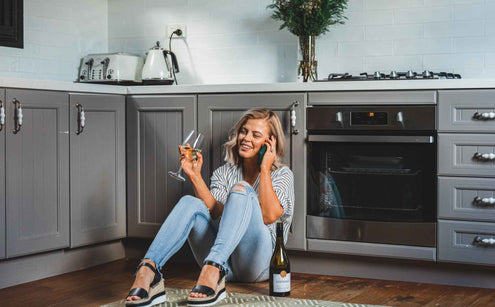 Women sitting on her kitchen floor drinking wine and on the phone