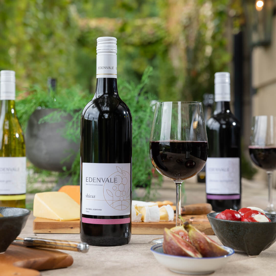 Two bottles of Edenvale non-alcoholic red wine on an outdoor table with two full glasses and a cheese platter