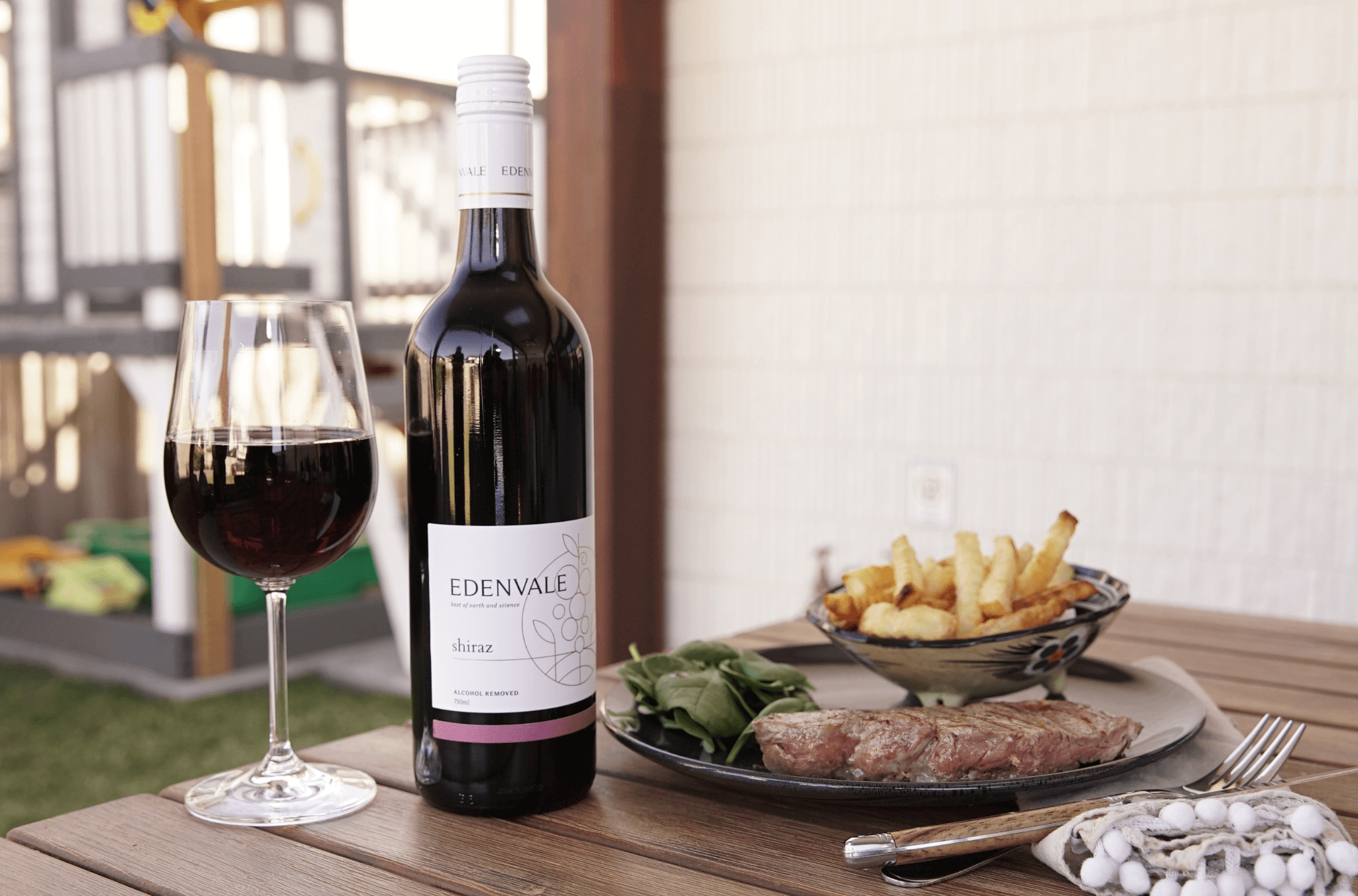 Glass of 3/4 full non-alcoholic red wine standing on a table next to a full bottle of Edenvale non-alcoholic Shiraz