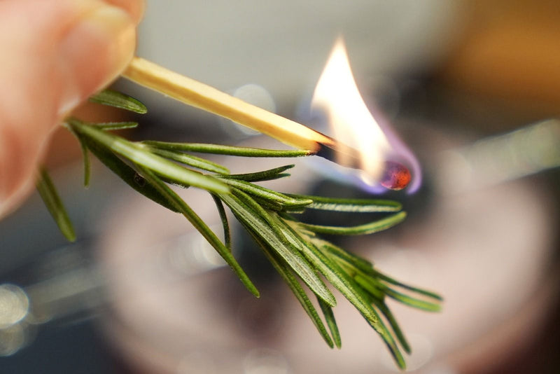Fresh rosemary being charred with a lit match to create a subtle, smoky aroma for the Black Cedar Sour Mocktail.