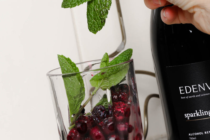 Close-up of a bottle of Edenvale Non-Alcoholic Sparkling Shiraz and a blender filled with blueberries, lime, and mint.
