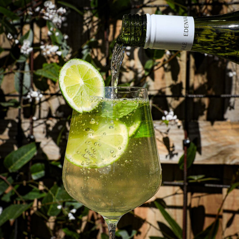 Edenvale Pinot Gris being poured into a glass of Mint and Citrus White Sangria mocktail laid out on marble, including sliced lemon and lime, fresh mint and ice