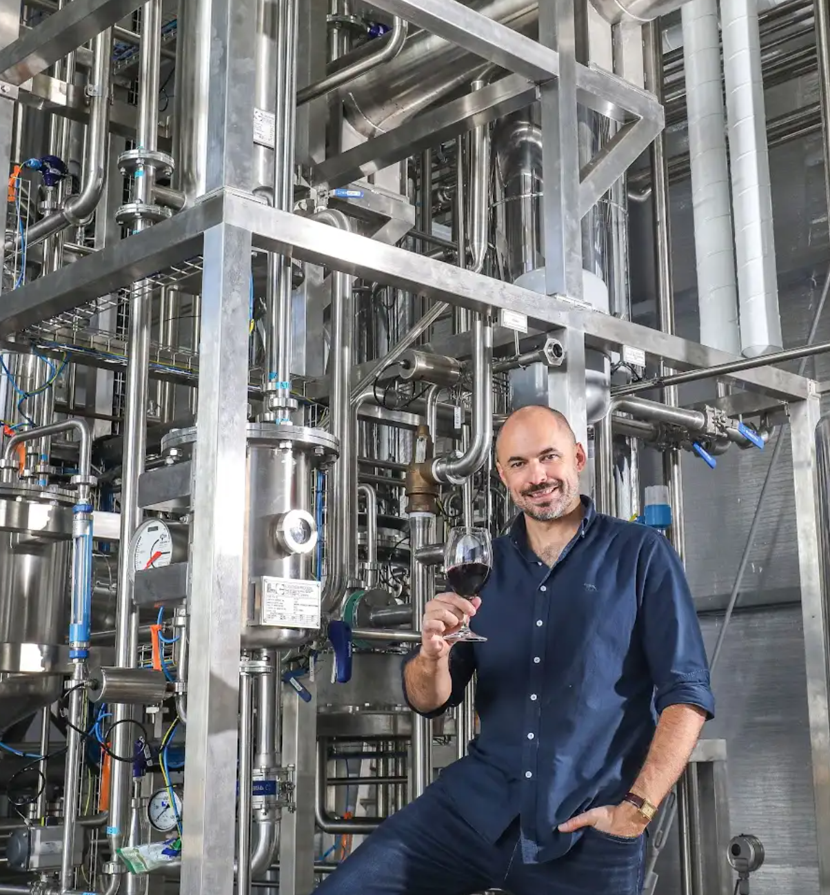 Edenvale winemaker standing in front of alcohol-removal GoLo heat-pump unit with a raised glass of non-alcoholic red wine