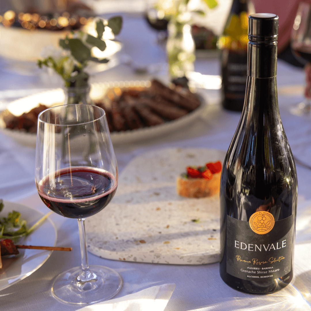 Glass of alcohol-removed red wine on an outdoor table next to a full bottle of Edenvale non-alcoholic GSM