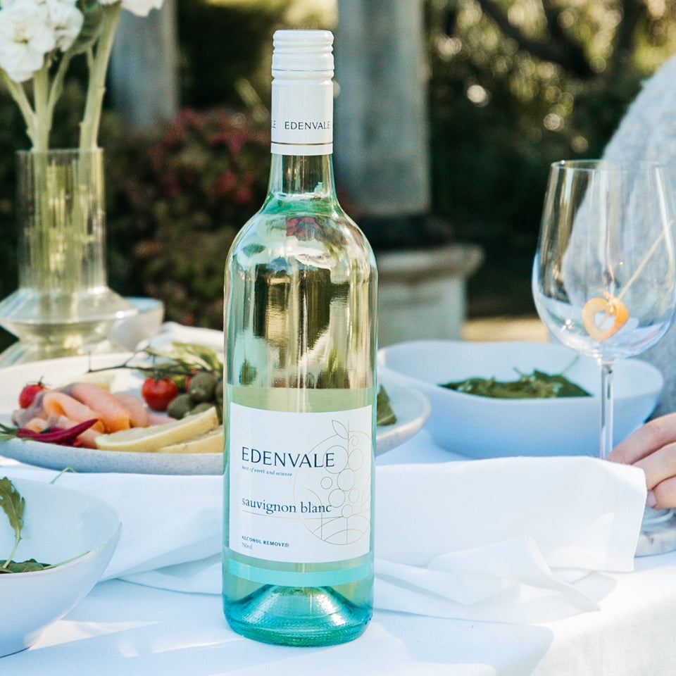 Full bottle of Edenvale Sauvignon Blanc on white linen tablecloth with empty glass and antipasto platter in the background