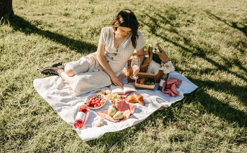 Woman picnicking on a rug laid over grass and styled with a  bottle of Edenvale Rose, fruit and croissants