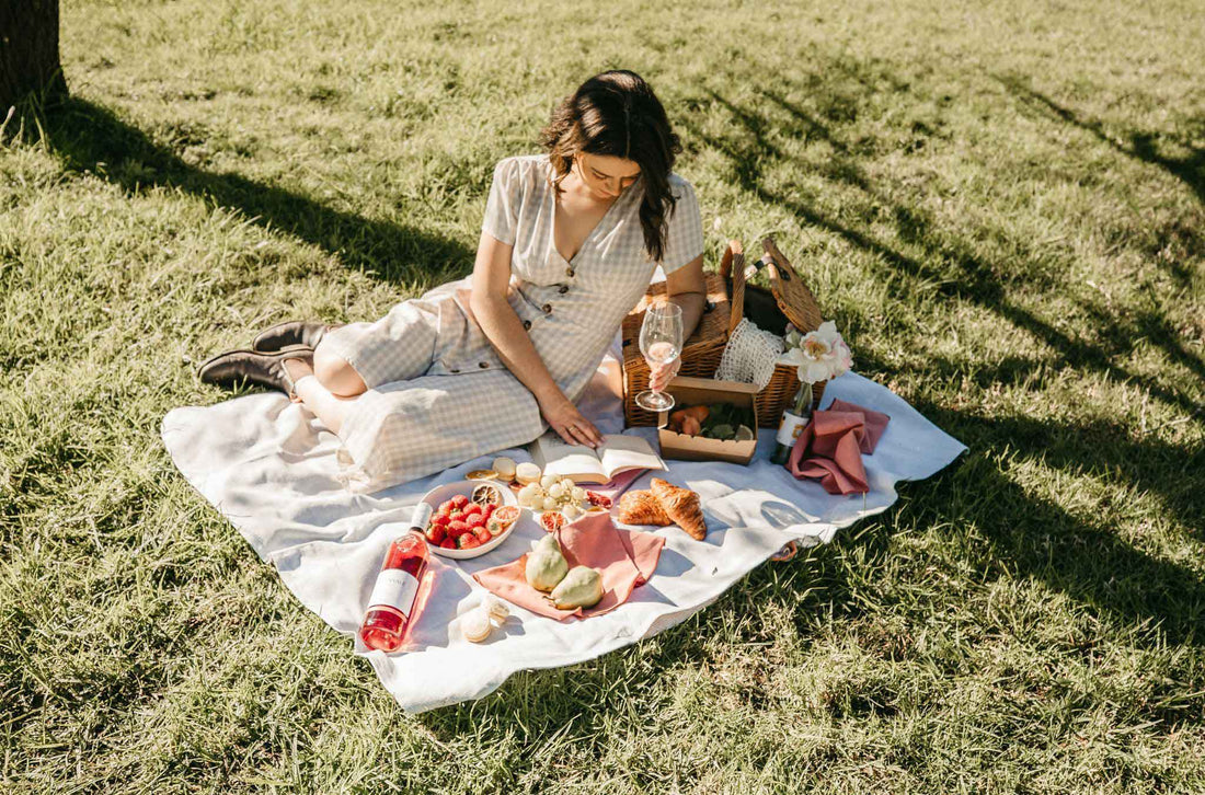 Woman picnicking on a rug laid over grass and styled with a  bottle of Edenvale Rose, fruit and croissants