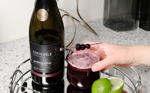 Blueberry Mojito mocktail in a stemless glassed garnished with blueberries next to a bottle of Edenvale Non-Alcoholic Sparkling Shiraz and fresh-cut limes.