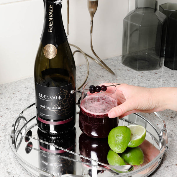 Blueberry Mojito mocktail in a stemless glassed garnished with blueberries next to a bottle of Edenvale Non-Alcoholic Sparkling Shiraz and fresh-cut limes.