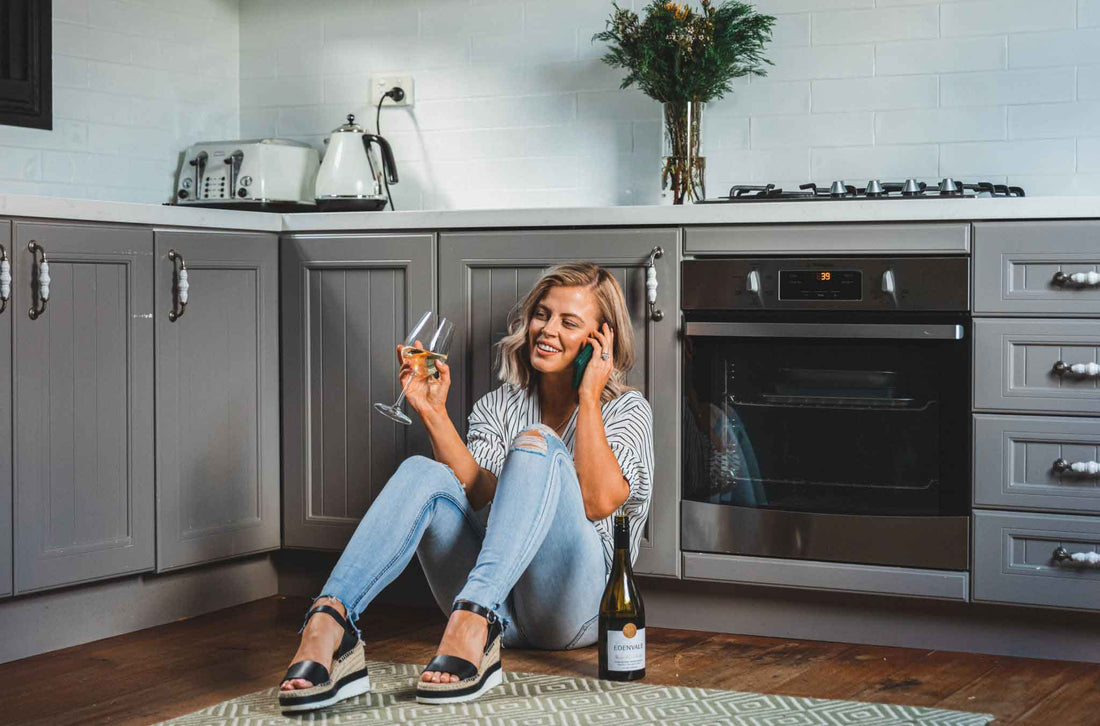Women sitting on her kitchen floor drinking wine and on the phone