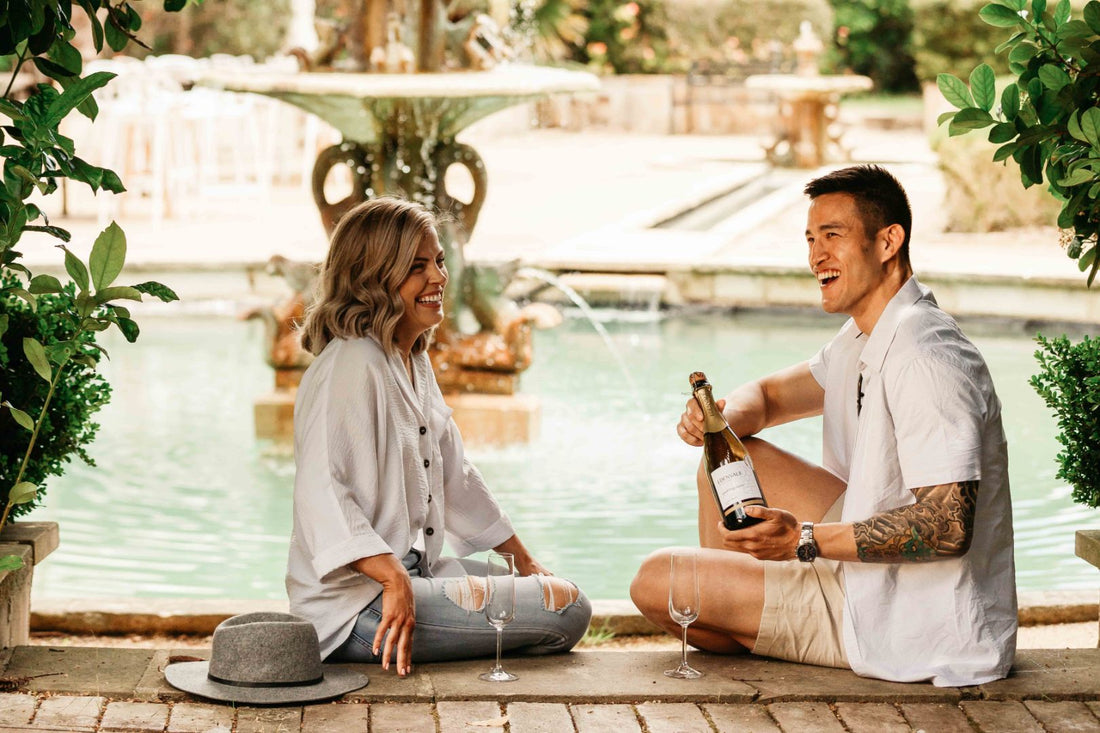 Couple sitting in front of a water fountain opening a bottle of non-alcoholic wine and celebrating Valentine's Day