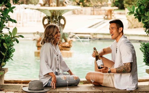 Couple sitting in front of a water fountain opening a bottle of non-alcoholic wine and celebrating Valentine's Day