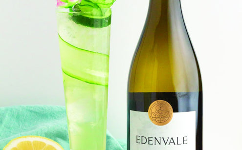  Cucumber Elderflower Spritz mocktail with cucumber garnish, cut lemon and blossoms beside a bottle of Edenvale Semillon Sauvignon Blanc