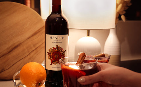 Woman’s hand around a Heart & Stone mocktail on a silver tray, with bottle of Edenvale Hearth and mood lighting in background