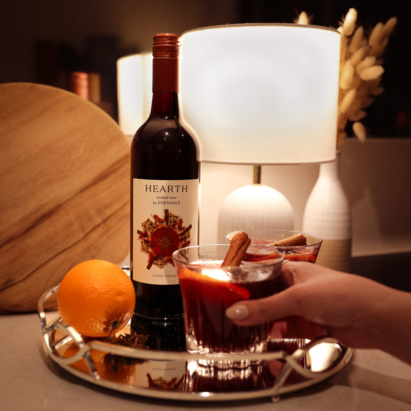 Woman’s hand around a Heart & Stone mocktail on a silver tray, with bottle of Edenvale Hearth and mood lighting in background
