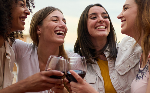 Four female friends outside in summer hugging and raising a toast with non-alcoholic red wine