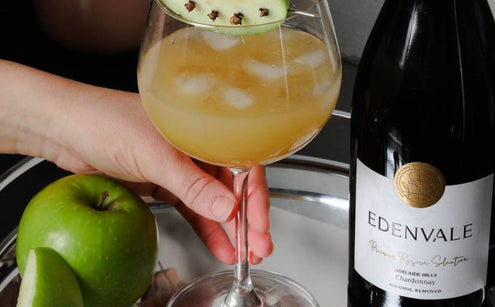 Golden Harvest Cooler mocktail in a stemmed glass garnished with green apple, served beside a bottle of Edenvale Chardonnay.