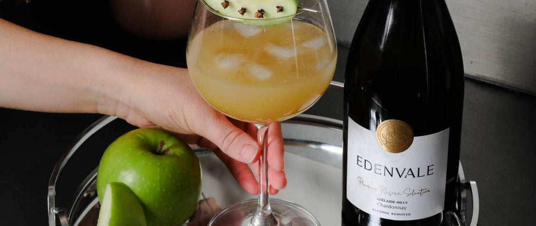 Golden Harvest Cooler mocktail in a stemmed glass garnished with green apple, served beside a bottle of Edenvale Chardonnay.