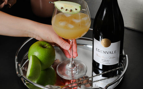 Golden Harvest Cooler mocktail in a stemmed glass garnished with green apple, served beside a bottle of Edenvale Chardonnay.