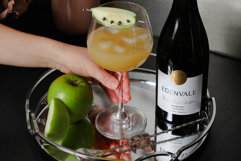 Golden Harvest Cooler mocktail in a stemmed glass garnished with green apple, served beside a bottle of Edenvale Chardonnay.
