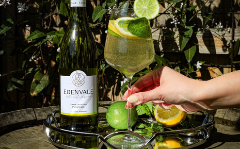 One glass of Mint and Citrus White Sangria mocktail served with a bottle of Edenvale Non-alcoholic Pinot Gris and fresh lime and lemon on a glass tray.