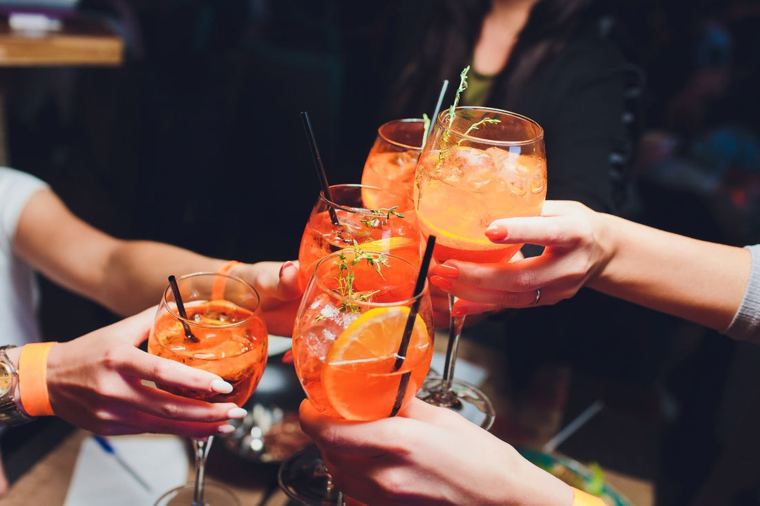 women raising  wine glasses of Aperol Spritz with citrus and herb garnish