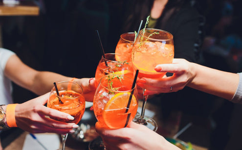 women raising  wine glasses of Aperol Spritz with citrus and herb garnish