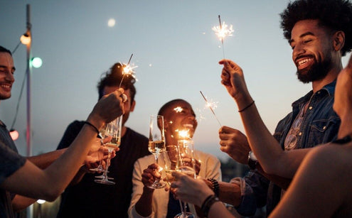 Group of friends at twilight hold celebratory sparklers and glasses of non-alcoholic sparkling wine