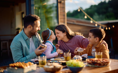 Parents and two children at outdoor table drinking, eating and having fun.