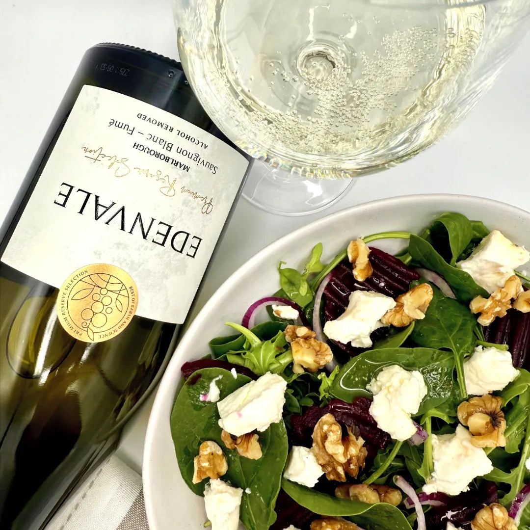 Aerial shot of a bottle of Edenvale Sauvignon Blanc - Fume lying down alongside a filled white wine glass and goat cheese, rocket and walnut salad