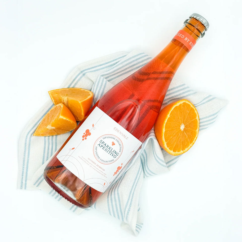 Bottle of Italian-style Sparkling Aperitivo lying flat on a linen teatowel with some cut oranges