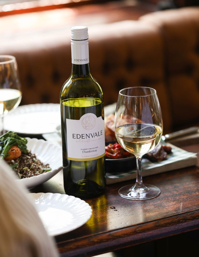 Bottle and glass of Edenvale non-alcoholic Chardonnay sitting on a timber surface with cheese, semi-dried tomatoes and green grapes.