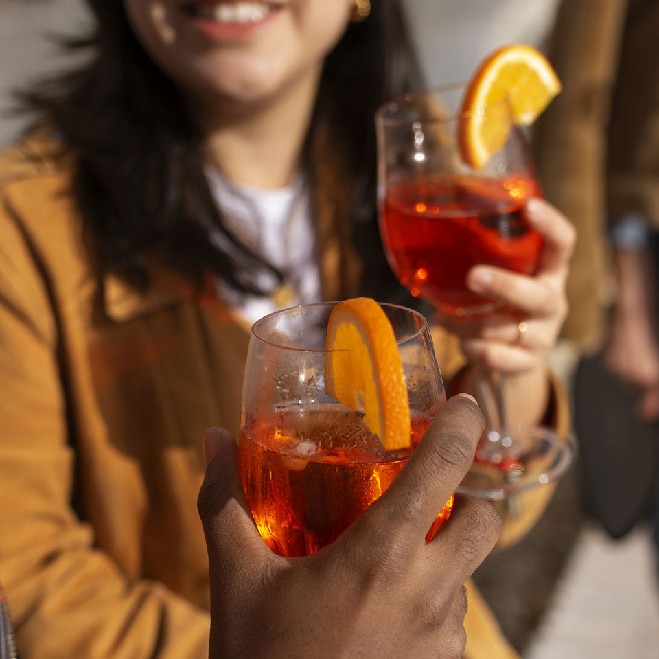 Close-up shot of an orange-infused botanicals drink wtih slice of orange. Woman holding same drink blurred in background