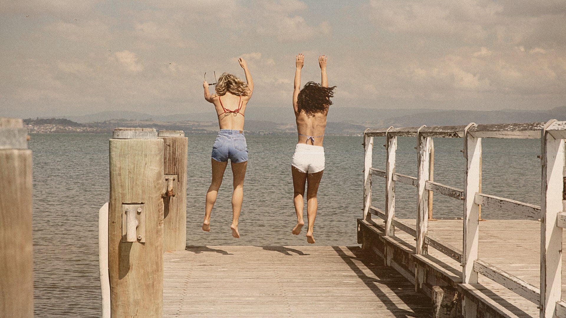 Two women jumping off the dock in swimsuits