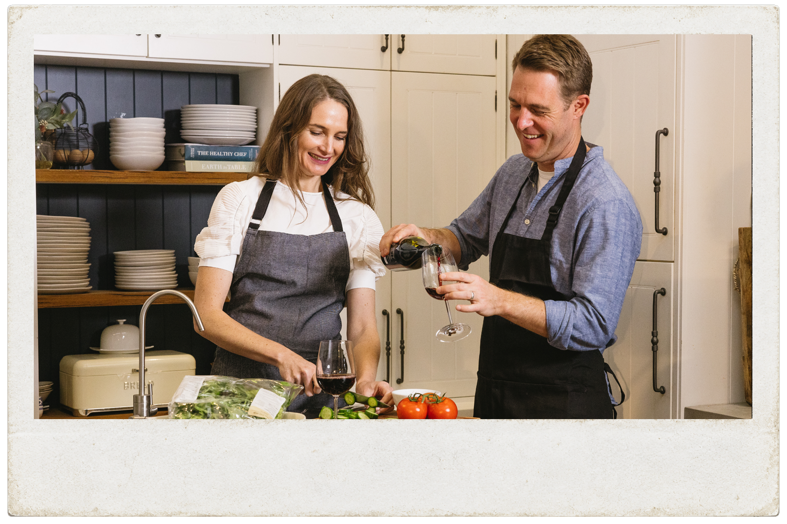 Man pouring Edenvale non-alcoholic red wine into a glass while a woman prepares fresh food at a kitchen bench