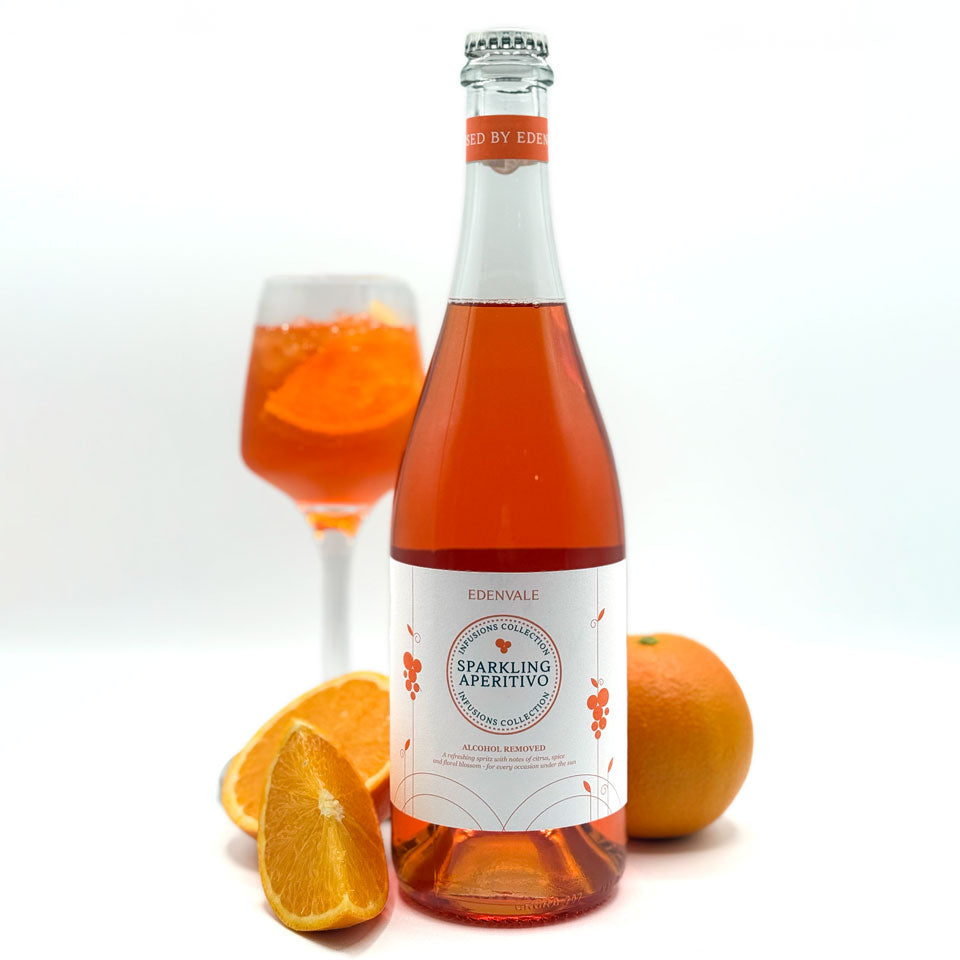 Full bottle of Edenvale Non-Alcoholic Sparkling Apertitivo next to full glass and cut oranges