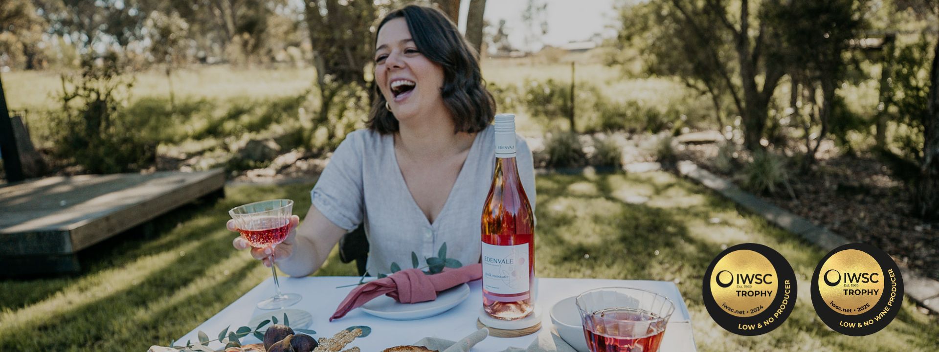 Woman enjoying a glass of rosé wine outdoors with IWSC logos displayed.