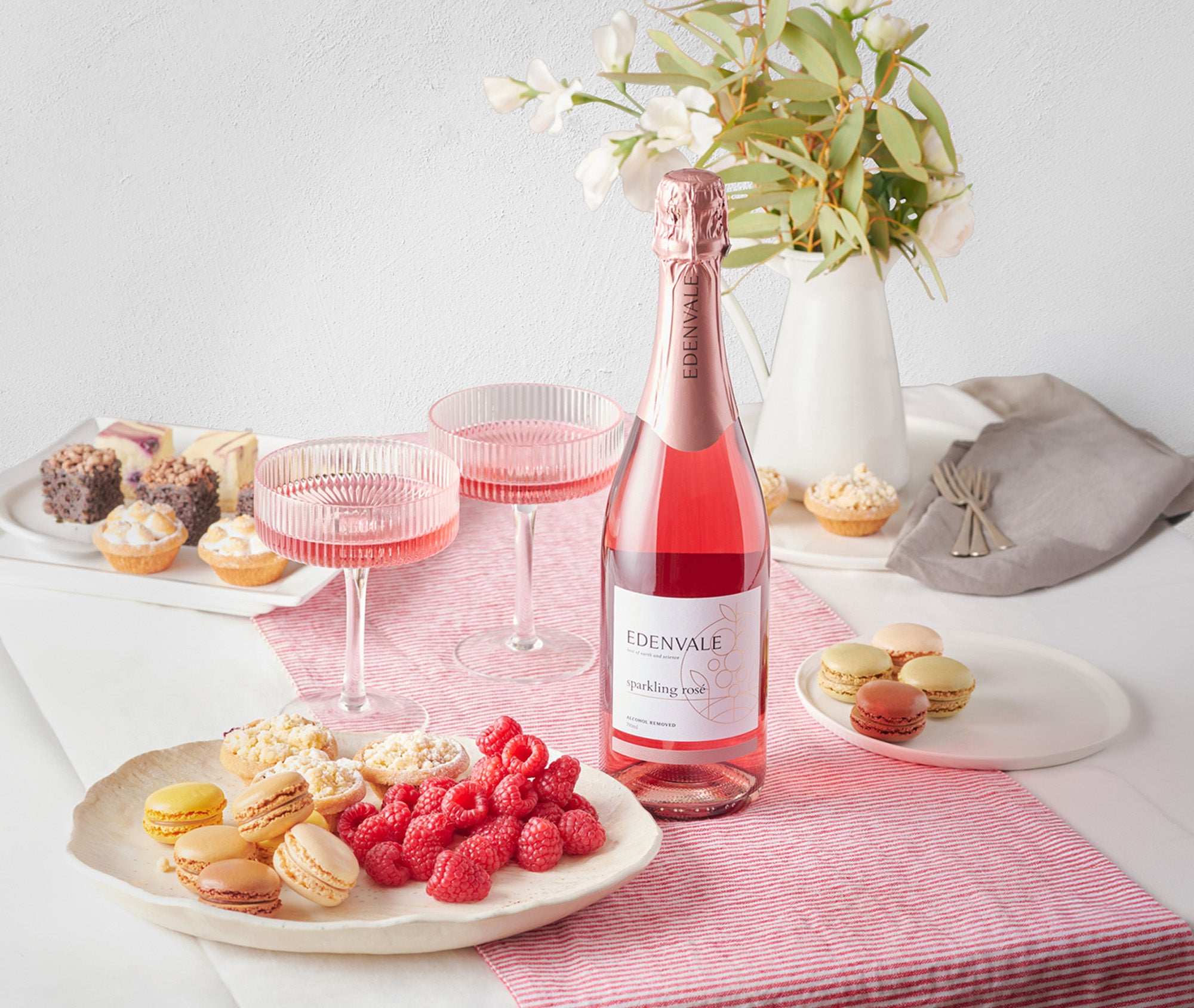 Edenvale alcohol-removed Sparkling Rosé bottle with two pink coupe glasses, fresh raspberries and macarons