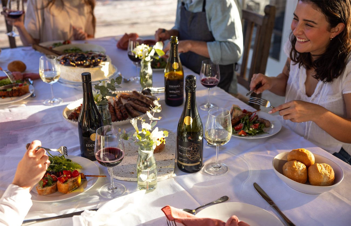 Friends sharing an outdoor meal with bottles and glasses of Edenvale non-alcoholic wine on the table