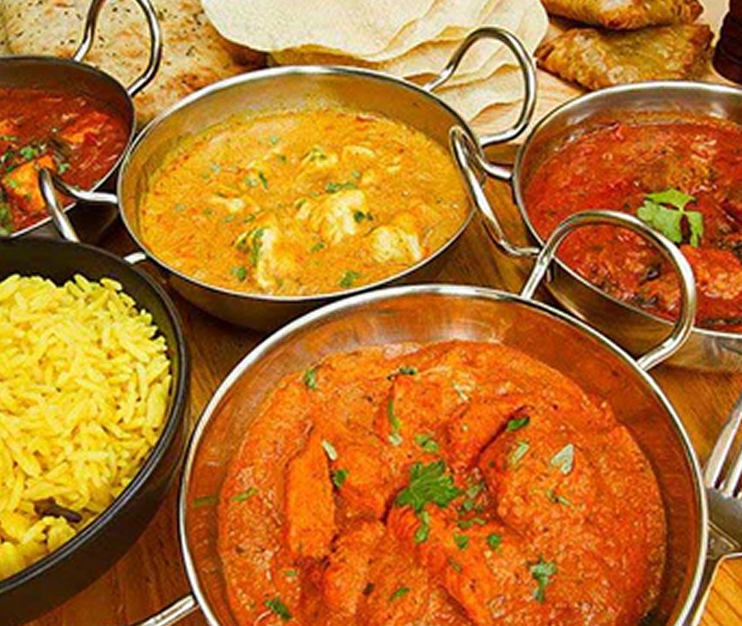 A variety of colourful Indian curries in classic silver serving dishes placed on a table 