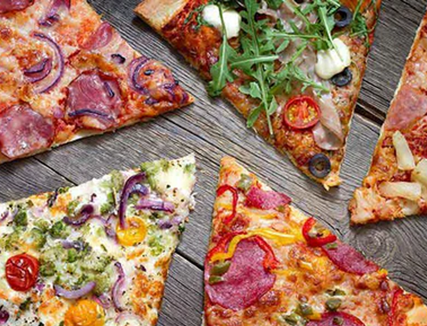 Aerial shot of a variety of triangular pizza slices on a timber table top