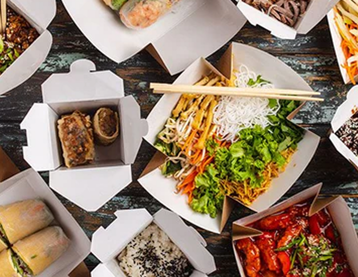 Aerial shot of a variety of take-away Thai dishes in classic cardboard containers with lids open and chopsticks randomly placed throughout